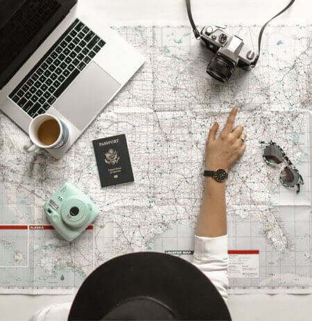 A person looking at a map determines where to go on their journey. They also have a passport, laptop computer, and camera. When embarking on a journey, you need a strategy, such as creating a successful content marketing strategy.