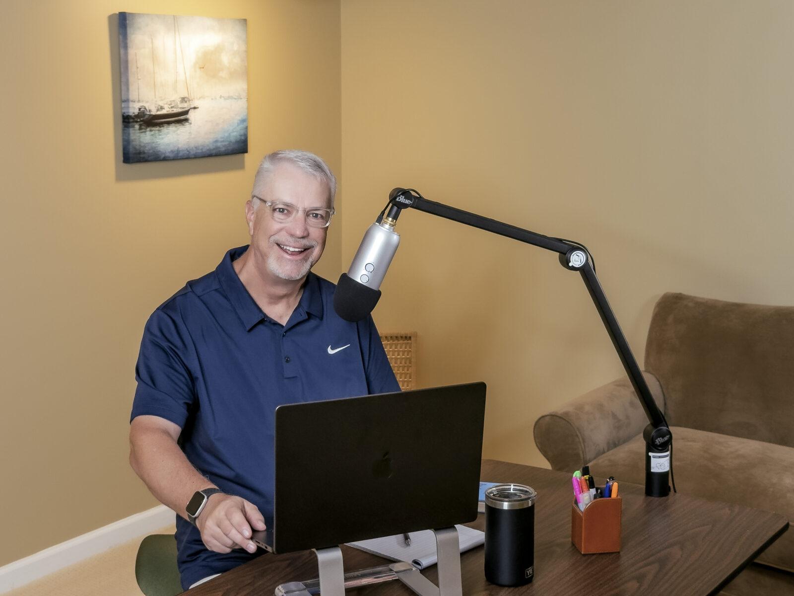 Doug sits at a table with a microphone and laptop, preparing to meet with a client.
